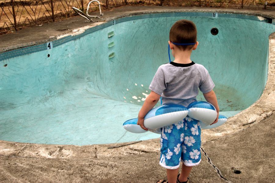 Kleiner Junge mit Schwimmreifen steht vor einem ausgelassenen, alten Swimmingpool